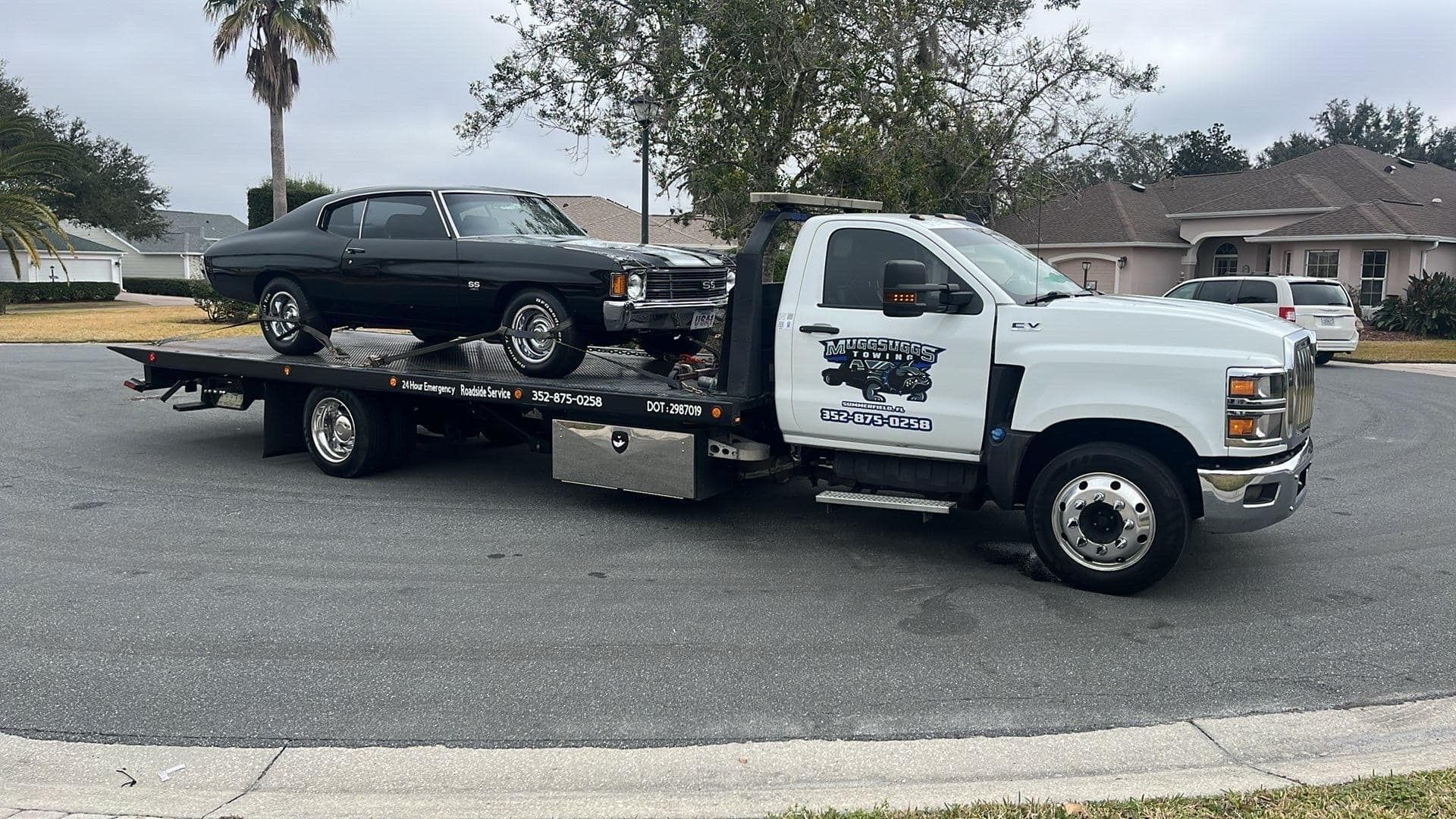 A black classic car on a white tow truck on a residential street.