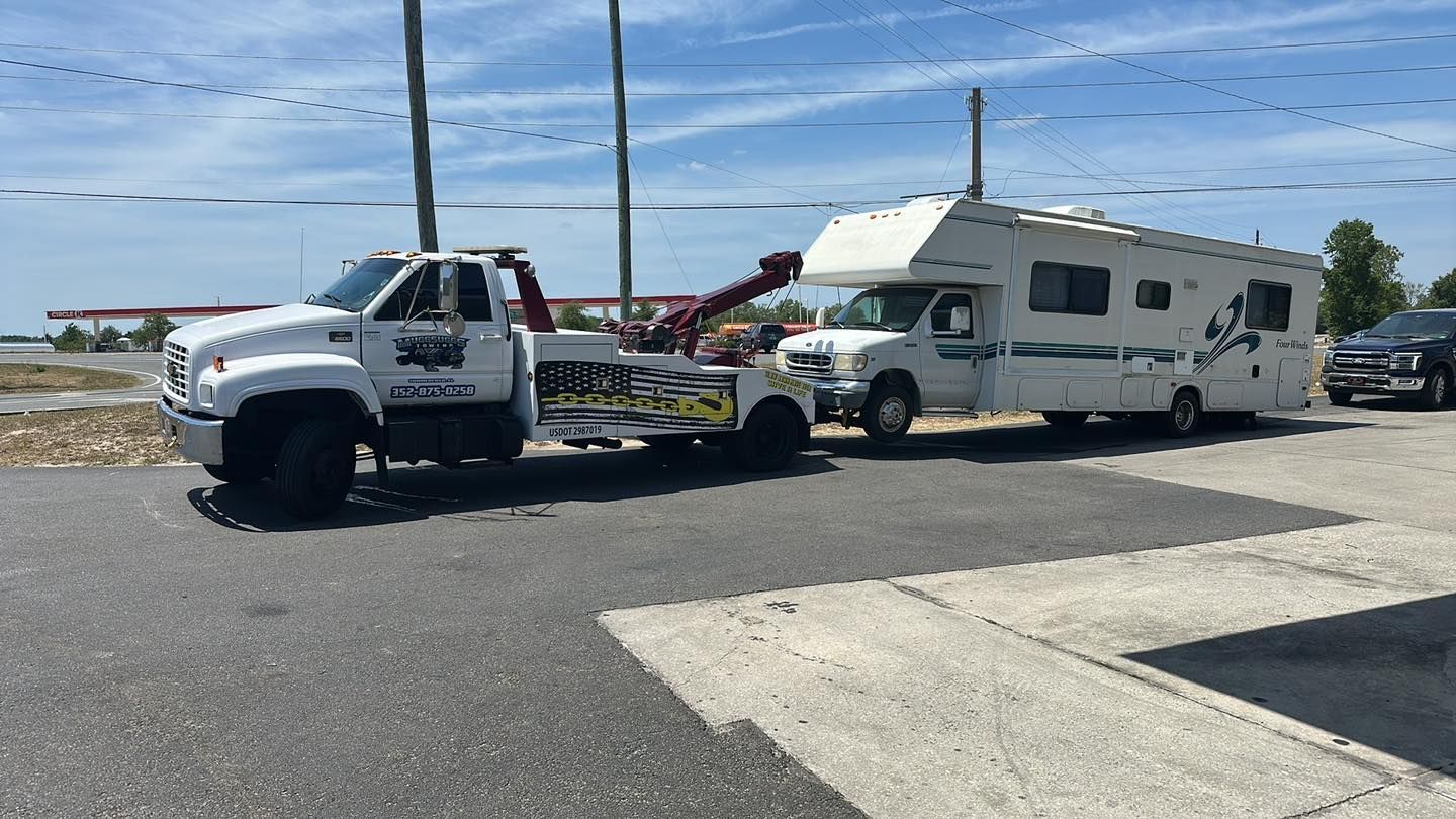 White tow truck pulling a white RV on a sunny day.