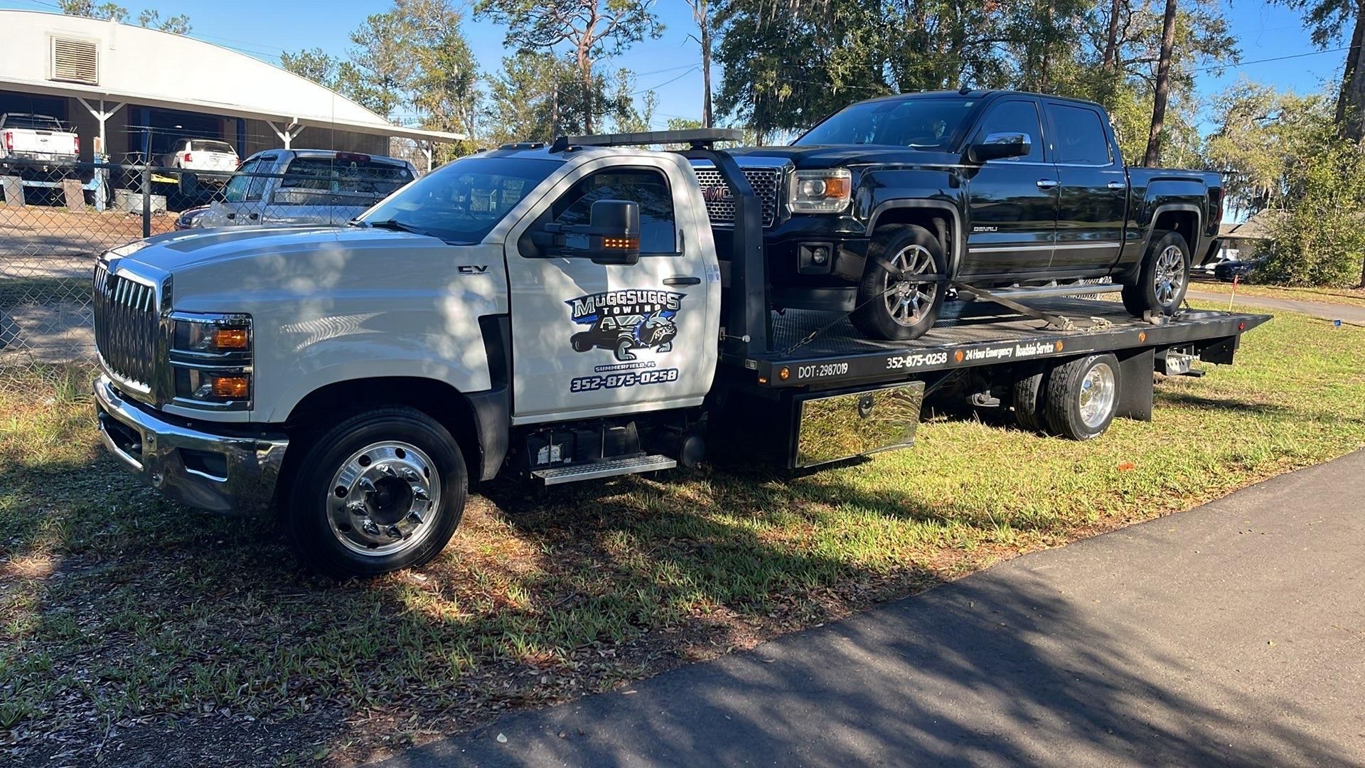 White tow truck carrying a black pickup truck on a sunny day.