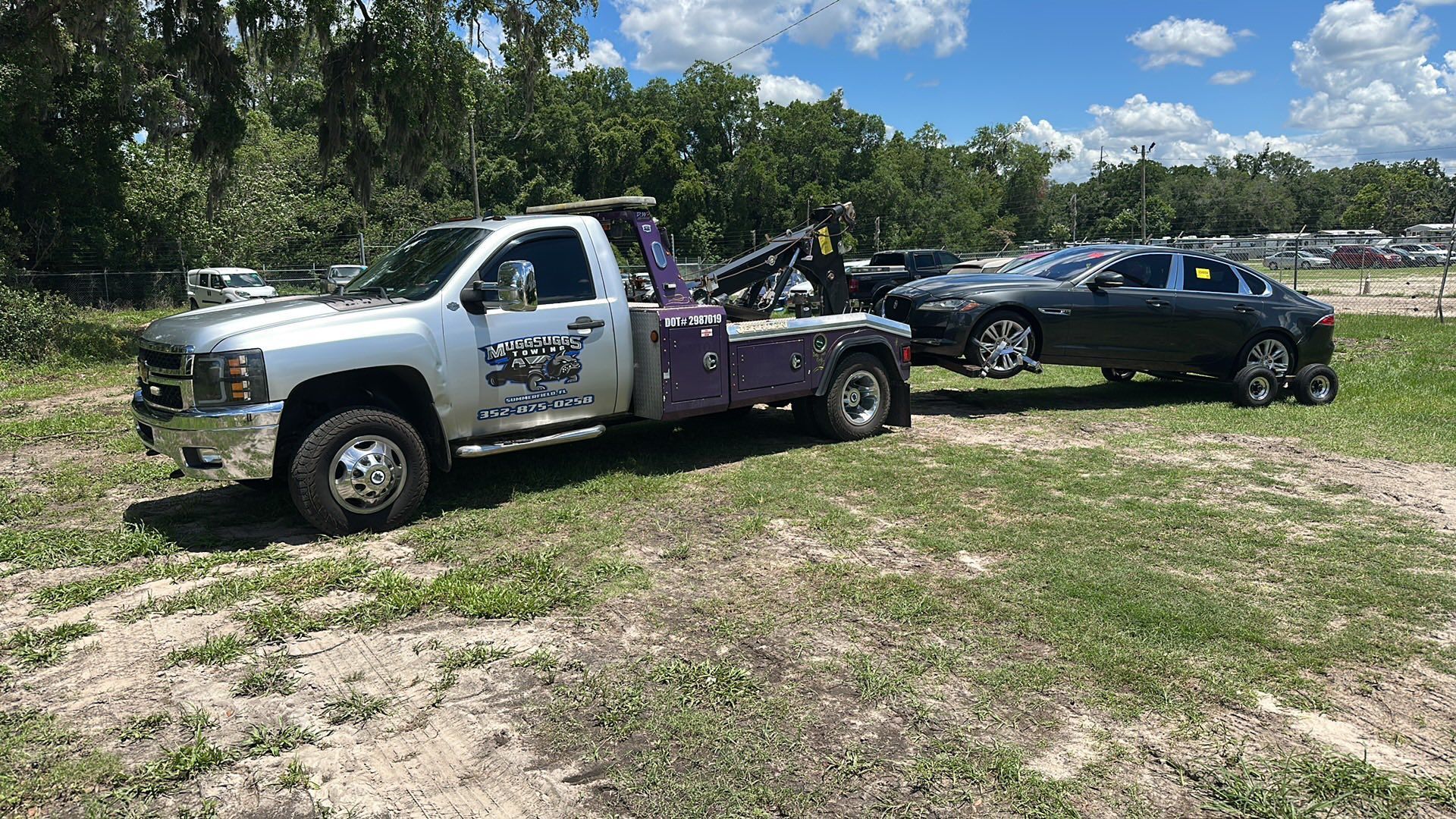 Tow truck towing a gray car on a grassy field.