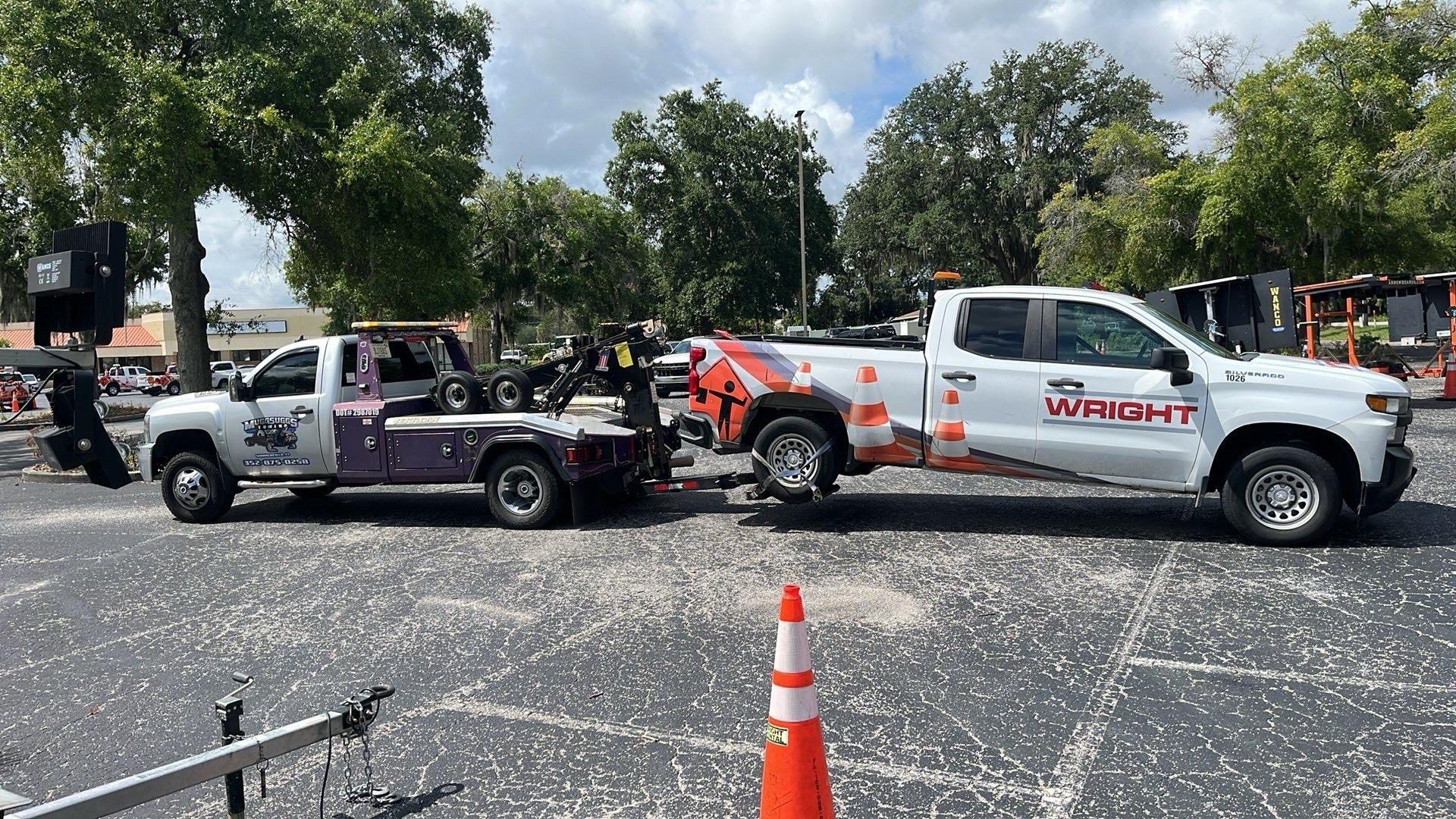 Two tow trucks are hooking up in a parking lot. One is white and the other purple.