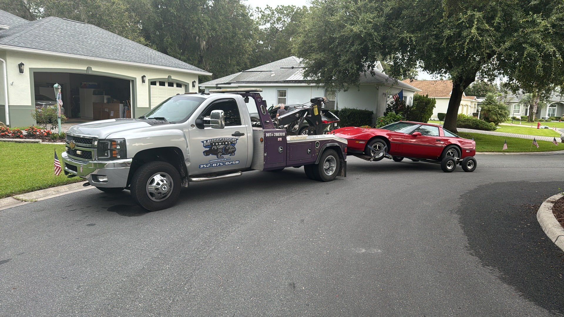 Tow truck towing a red car down a residential street.