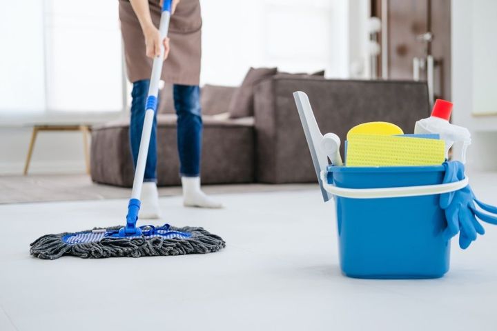 A woman is mopping the floor in a living room next to a bucket of cleaning supplies.