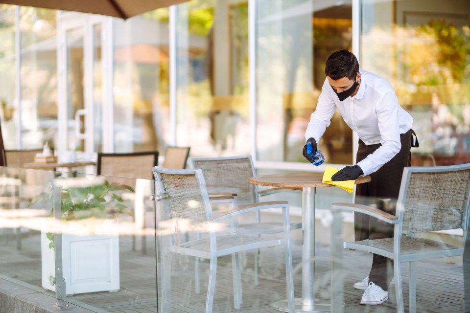 A man is cleaning a table outside of a restaurant.