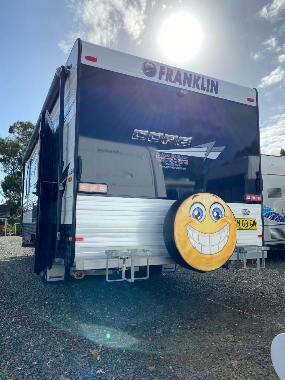 A RV With A Smiley Face On The Tire Cover Is Parked In A Gravel Lot — Great Lakes Caravans In Nabiac, NSW