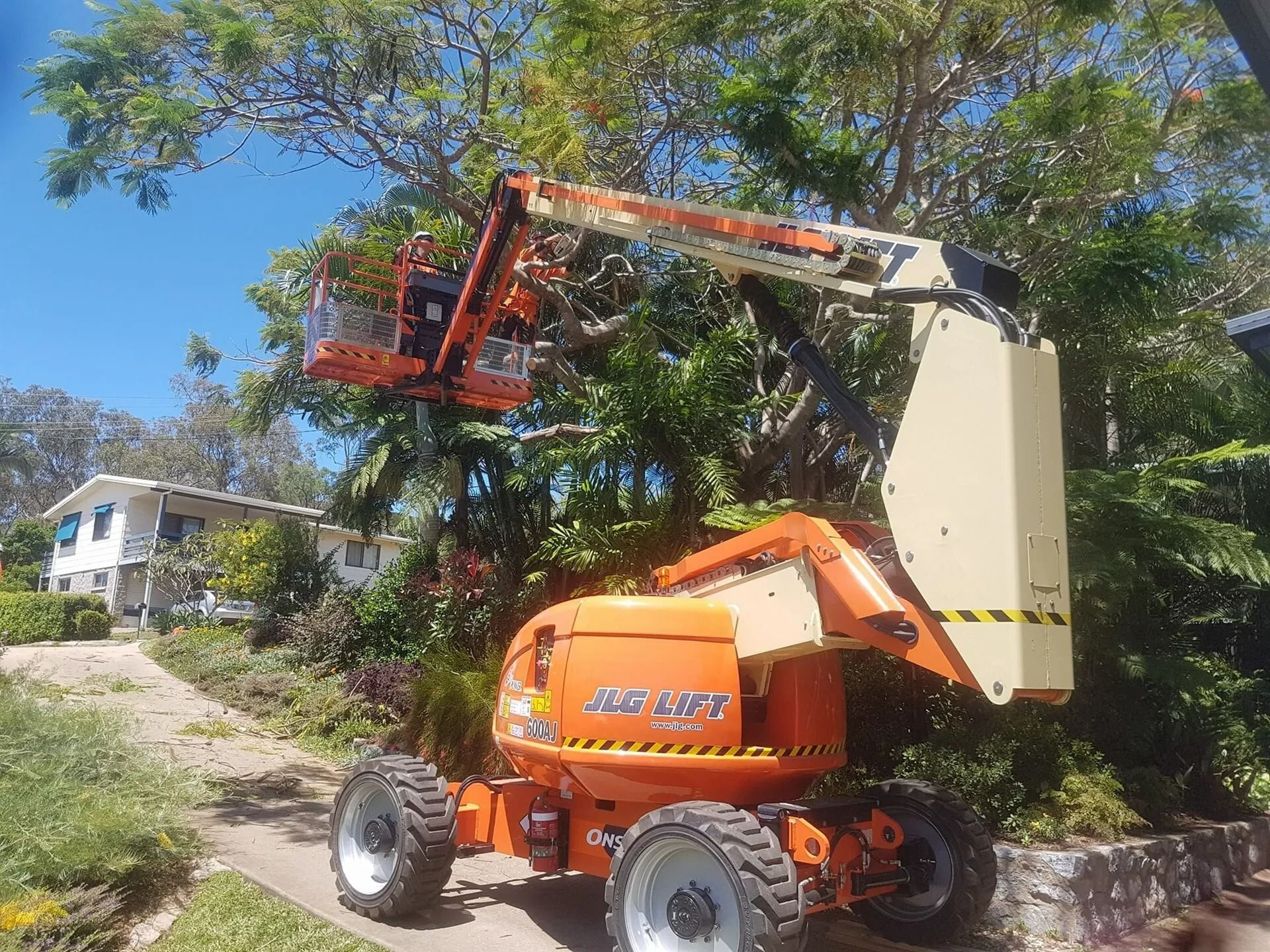 Orange Cherry Picker Trimming Tree Branches Near a House on a Sunny Day — Barlows Tree Services in Rockhampton, QLD