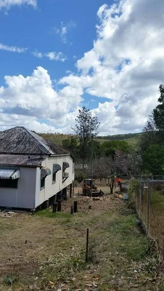 Small White House With a Gray Roof Beside a Grassy Yard and Trees — Barlows Tree Services in Rockhampton, QLD