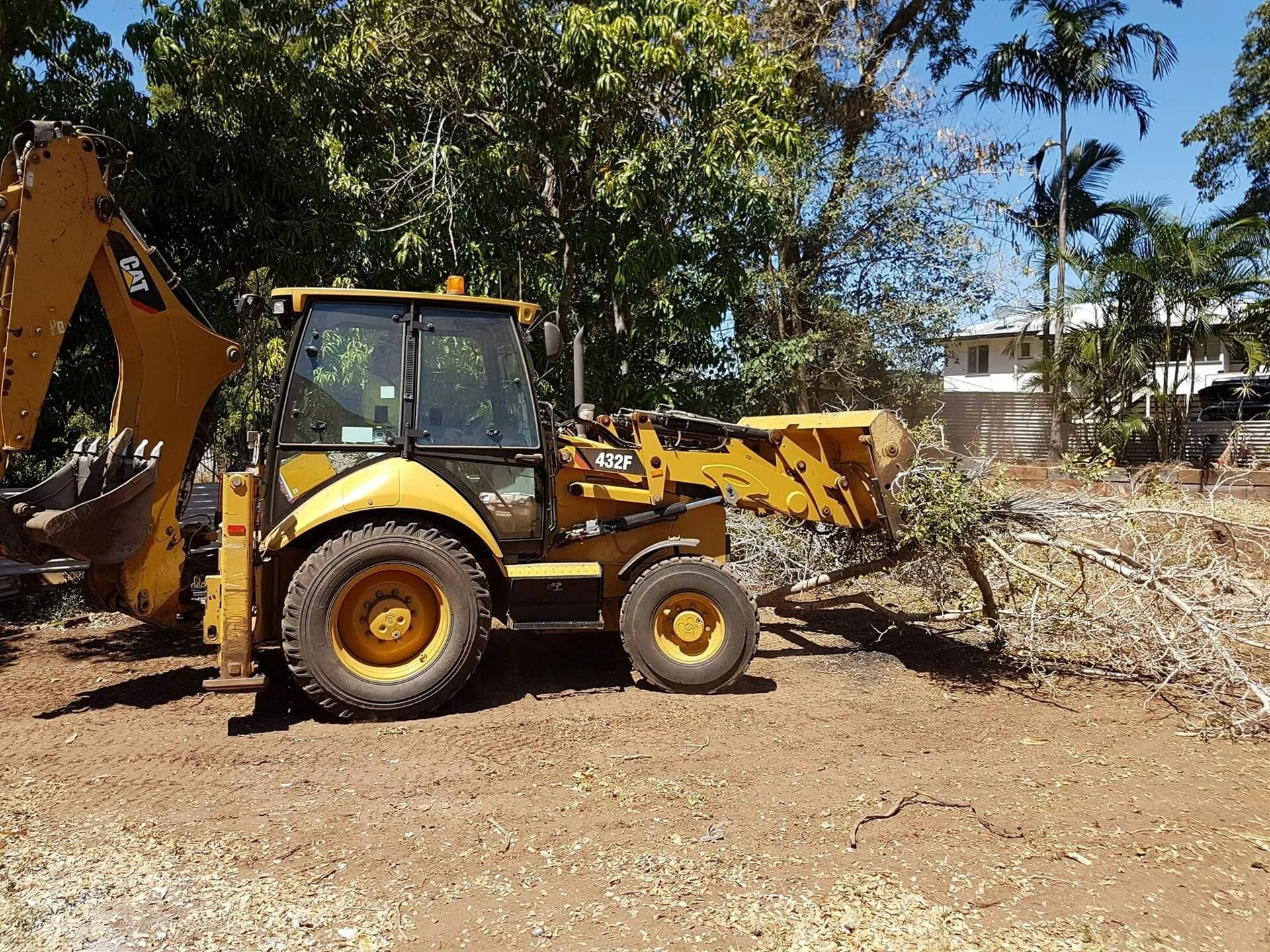Yellow Cat Backhoe Clearing Brush on a Dirt Lot — Barlows Tree Services in Rockhampton, QLD
