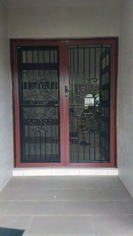 A door with a wrought iron grill on it is sitting on a tiled floor.
