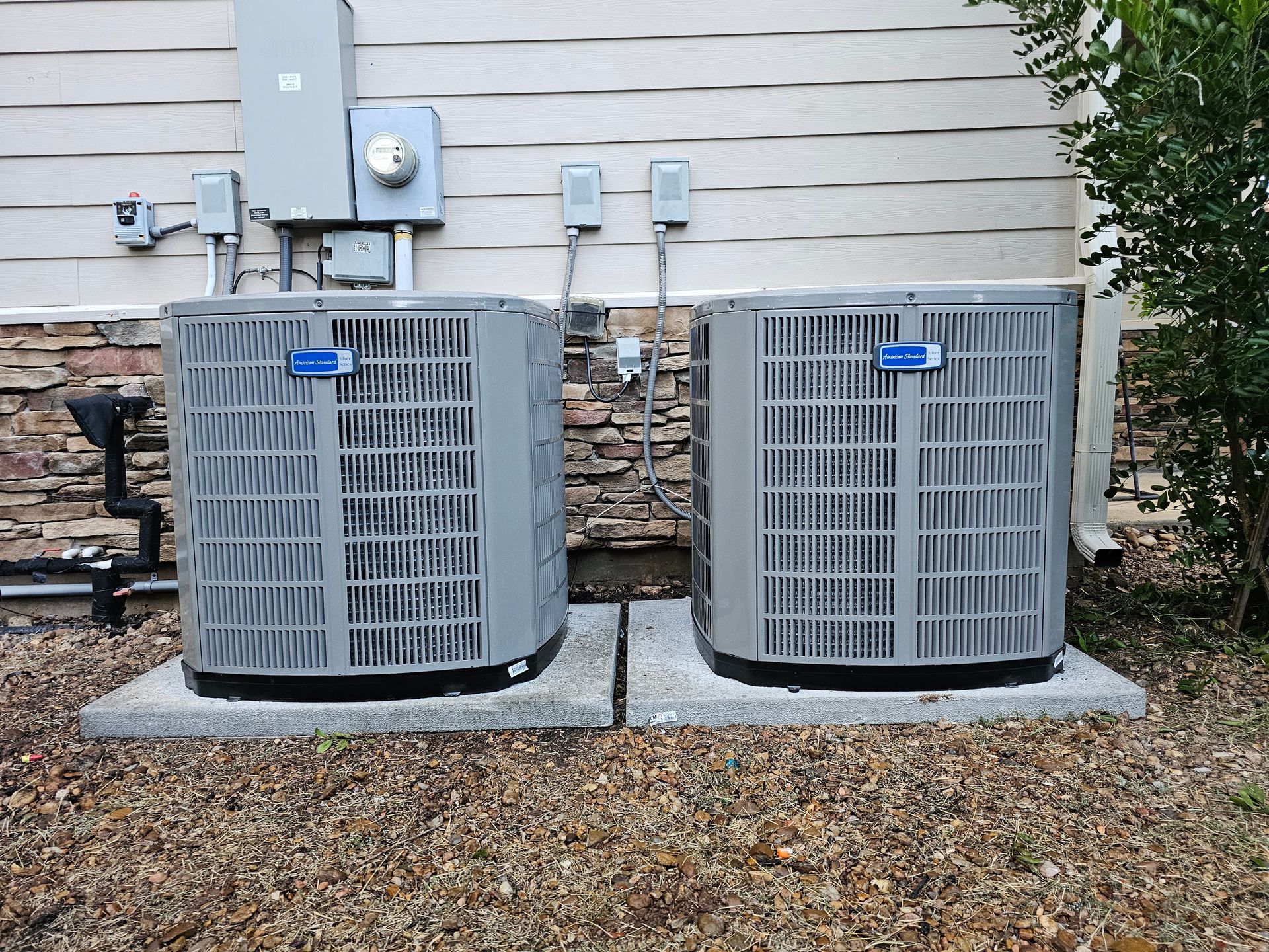 Two air conditioners are sitting next to each other outside of a house.