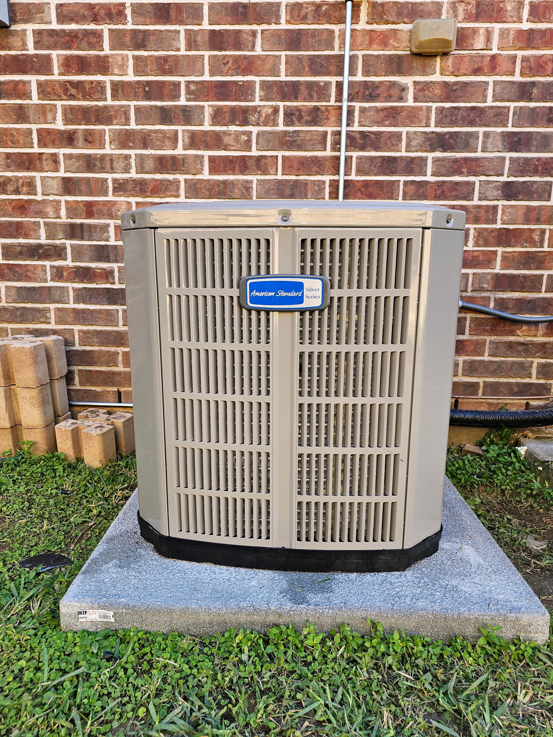 An air conditioner is sitting on top of a concrete platform in front of a brick wall.
