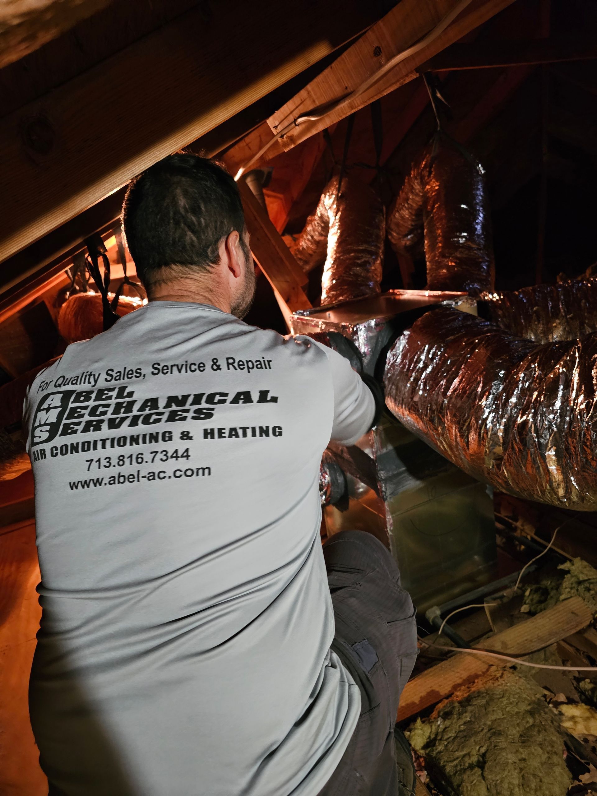 A man is working on an air duct in an attic.