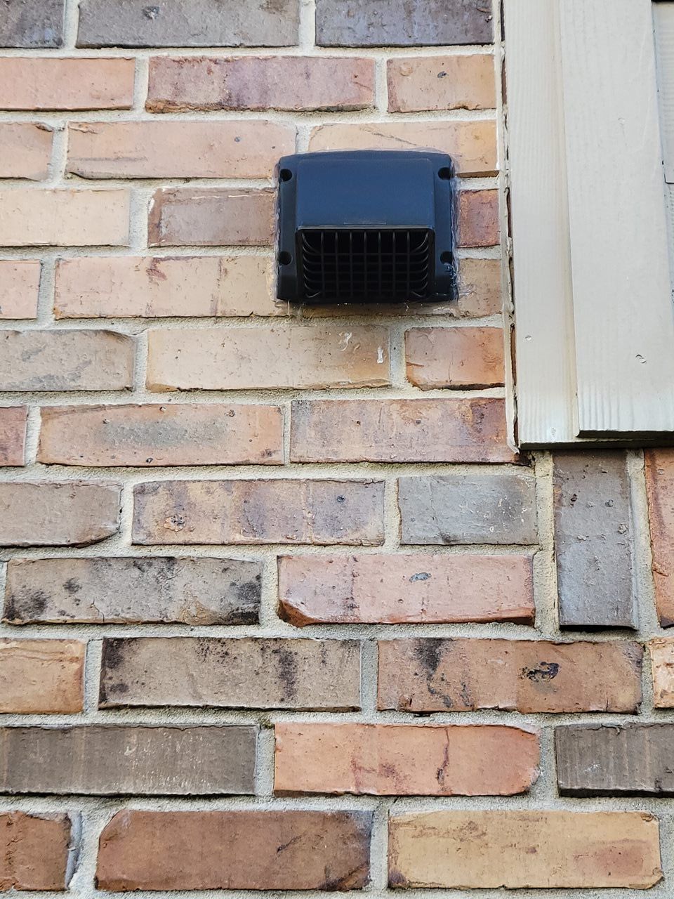 A brick wall with a black vent on it