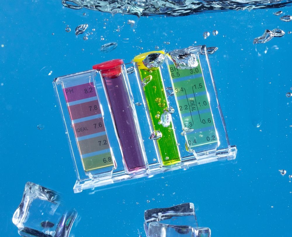 Test strips submerged in blue water, showing color changes for pH, chlorine, and bromine levels.