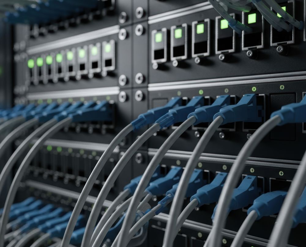 Network server rack with many blue Ethernet cables plugged in. Green lights indicate activity.