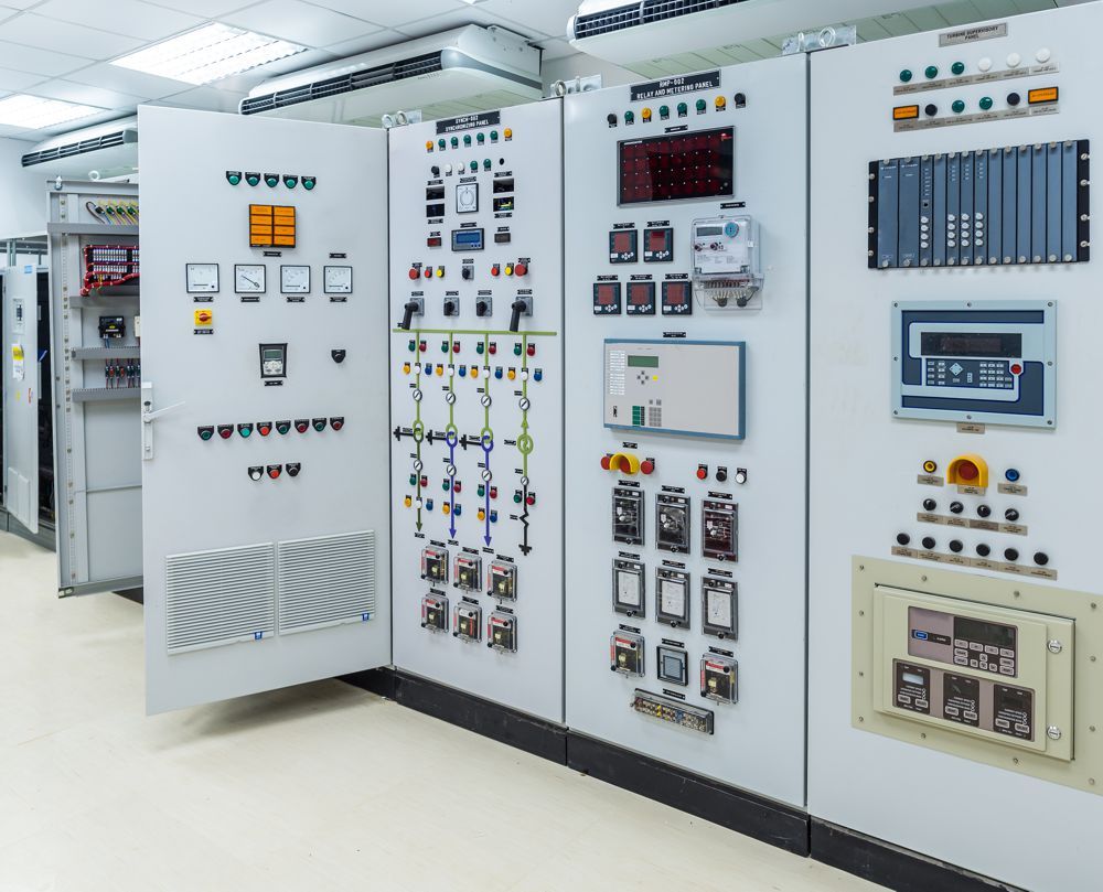 Control panels with numerous buttons, switches, and displays in a clean, brightly lit room.