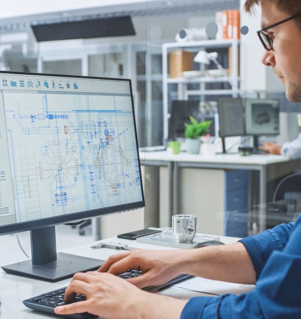 Man working on computer with engineering schematics, in modern office setting.