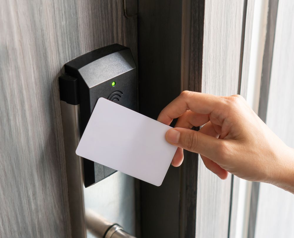 Person swiping a white card to unlock a door with a black card reader, in a wooden door frame.