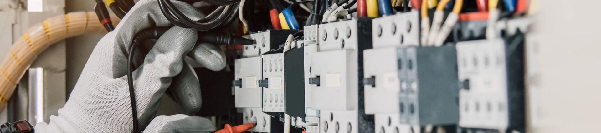 A gloved hand working on electrical wiring in an electrical panel.