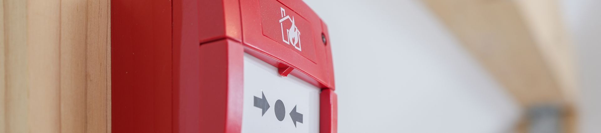 Red fire alarm on a light brown wooden wall, white background.