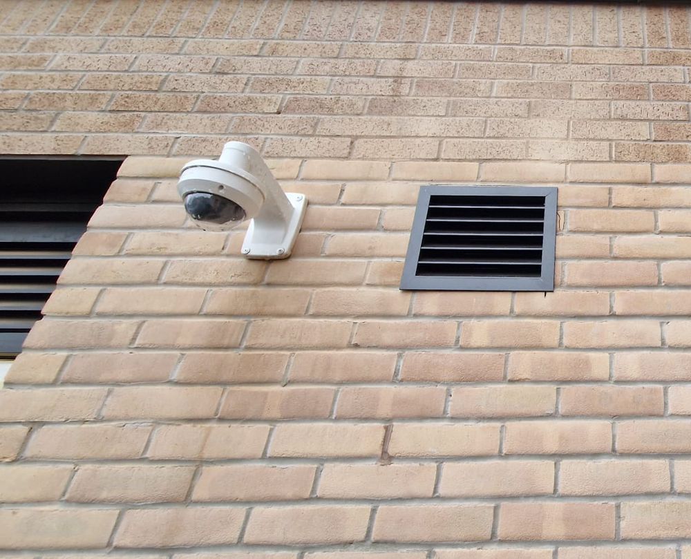 Security camera mounted on a brick wall next to a vent.