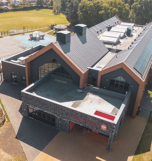 Modern building with a gray stone facade, flat roof, and playground in the background.