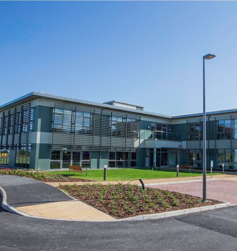 Modern two-story building with large windows and landscaping under a clear blue sky.