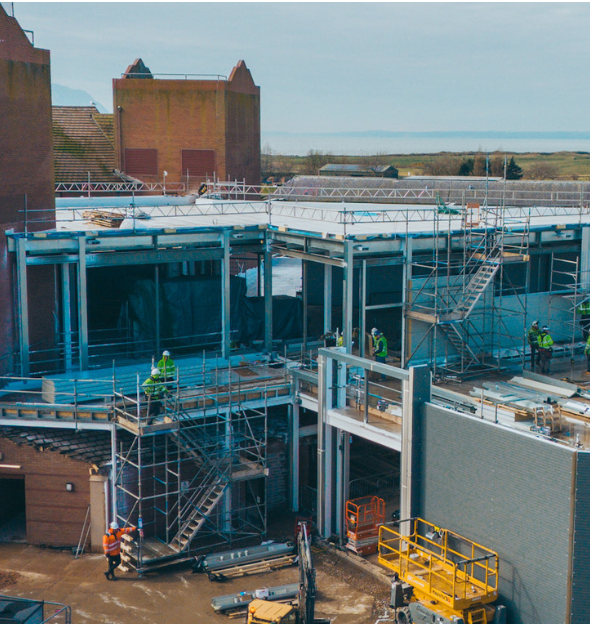 Construction site with steel framework. Workers in safety vests, scaffolding, and partially built buildings.