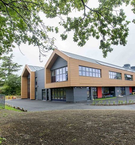 Modern school building with wooden siding, large windows, and a black paved entrance.