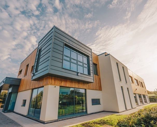 Modern building with glass windows, wood paneling, and a gray metal facade against a cloudy sky.