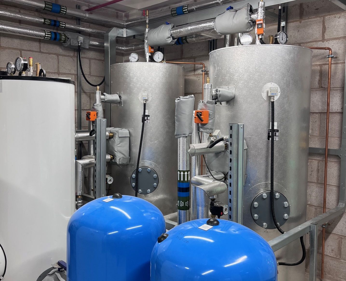 Industrial water tanks and pipes, with pressure gauges, in a mechanical room.