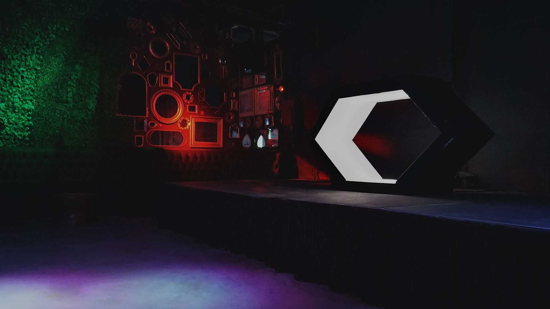 A dark, futuristic room with a glowing white portal, lit by red and green lights.