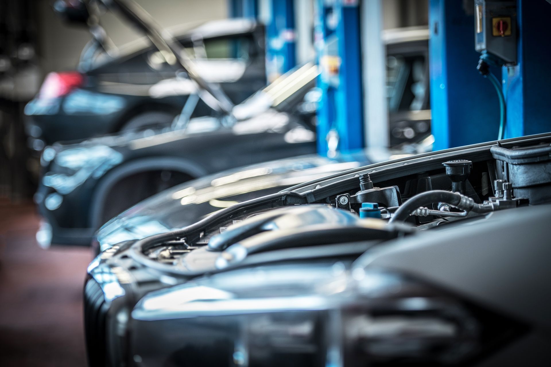 A row of cars are parked in a garage with their hoods open.