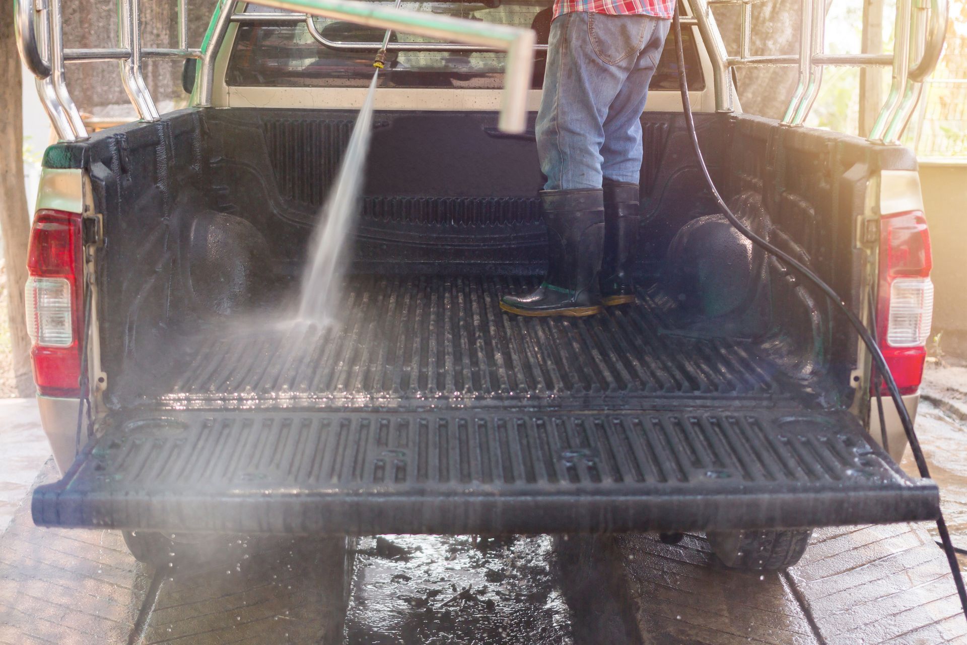A man is cleaning the back of a truck with a high pressure washer.