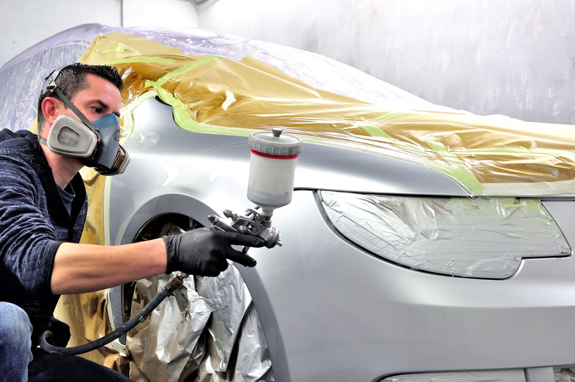 A man wearing a mask is spray painting a car.