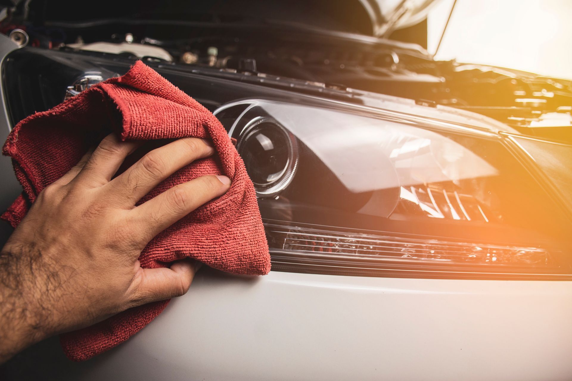 A person is cleaning the headlight of a car with a towel.