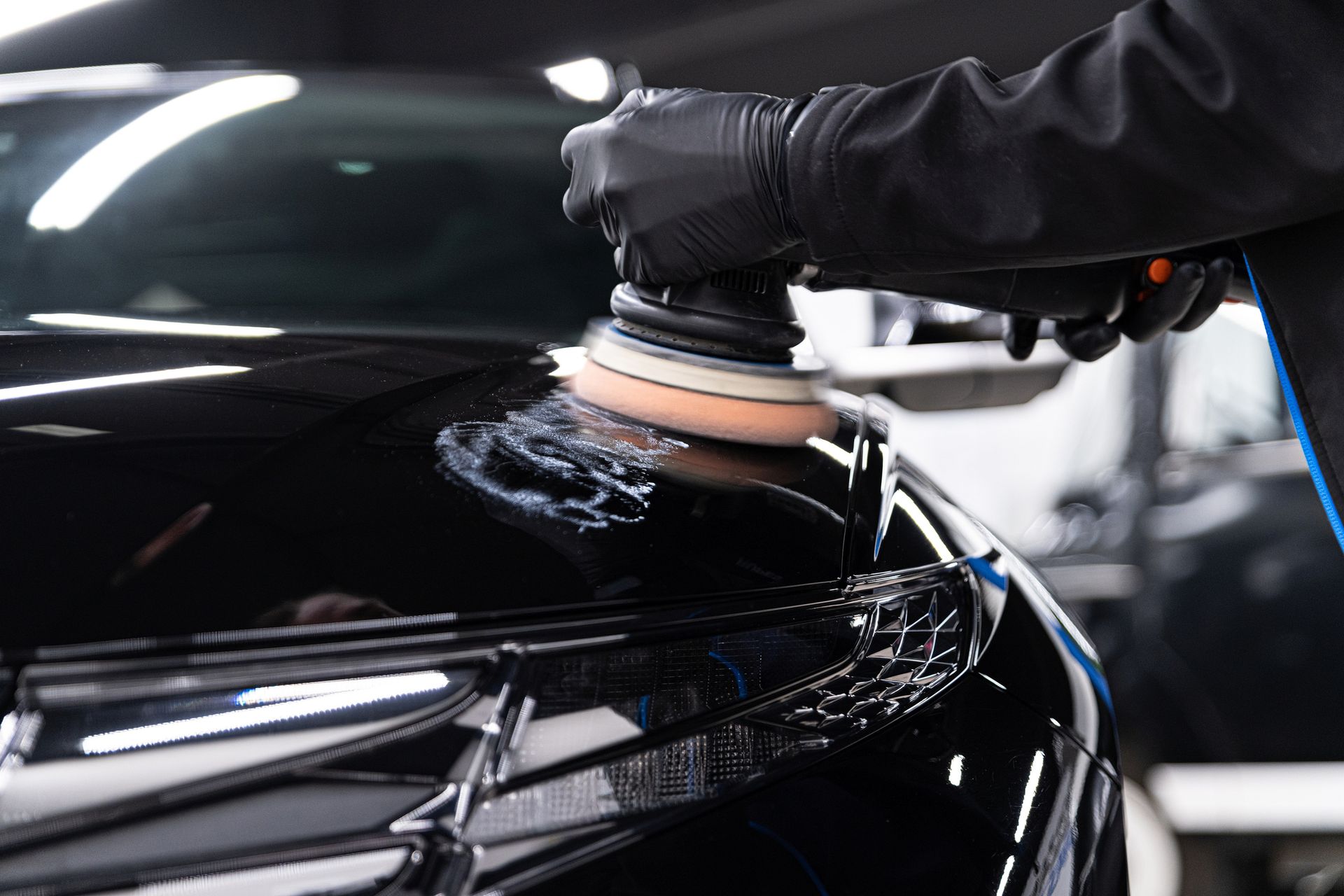 A person is polishing a black car with a machine.
