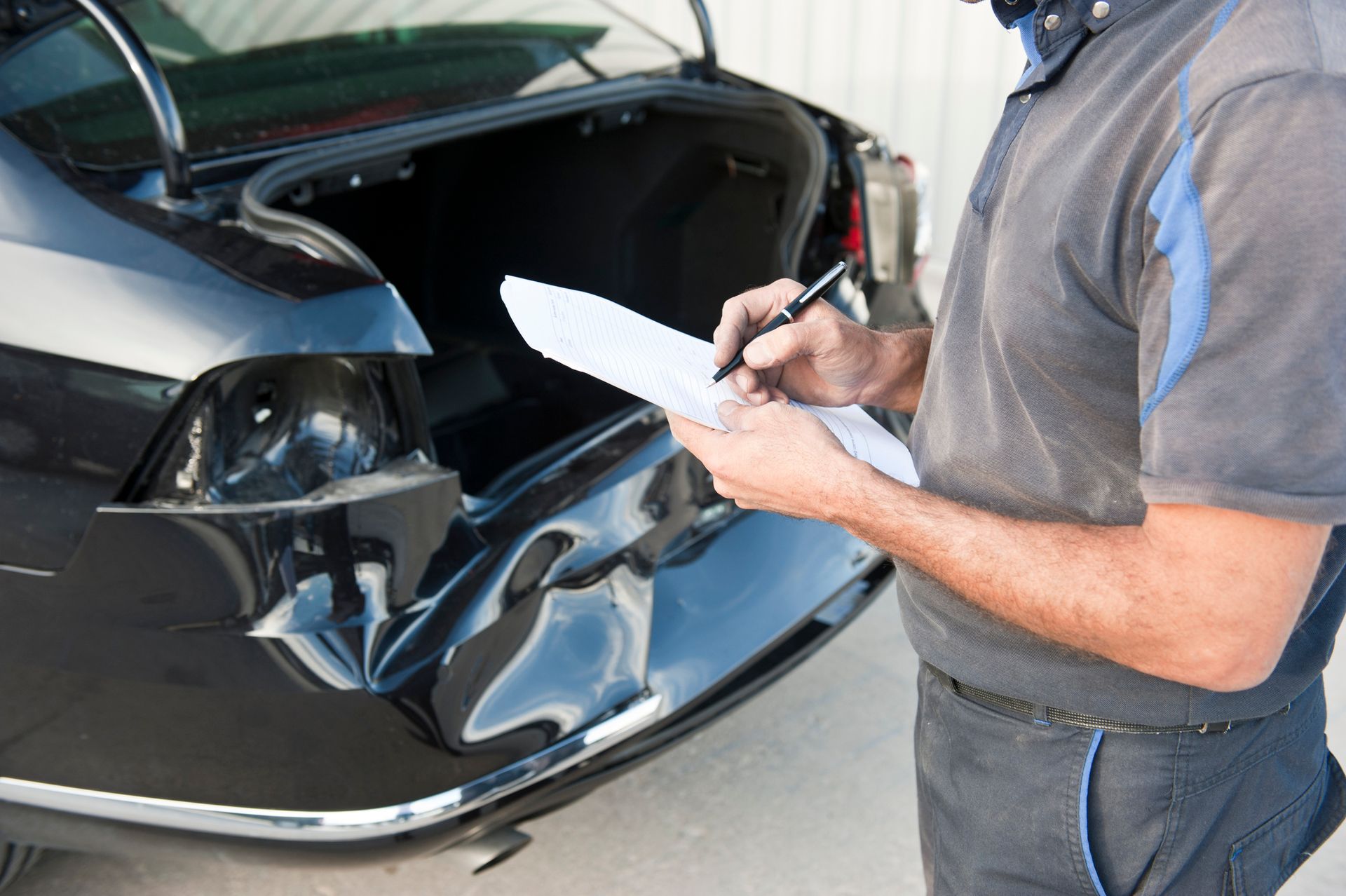 A man is writing on a piece of paper in front of a damaged car.