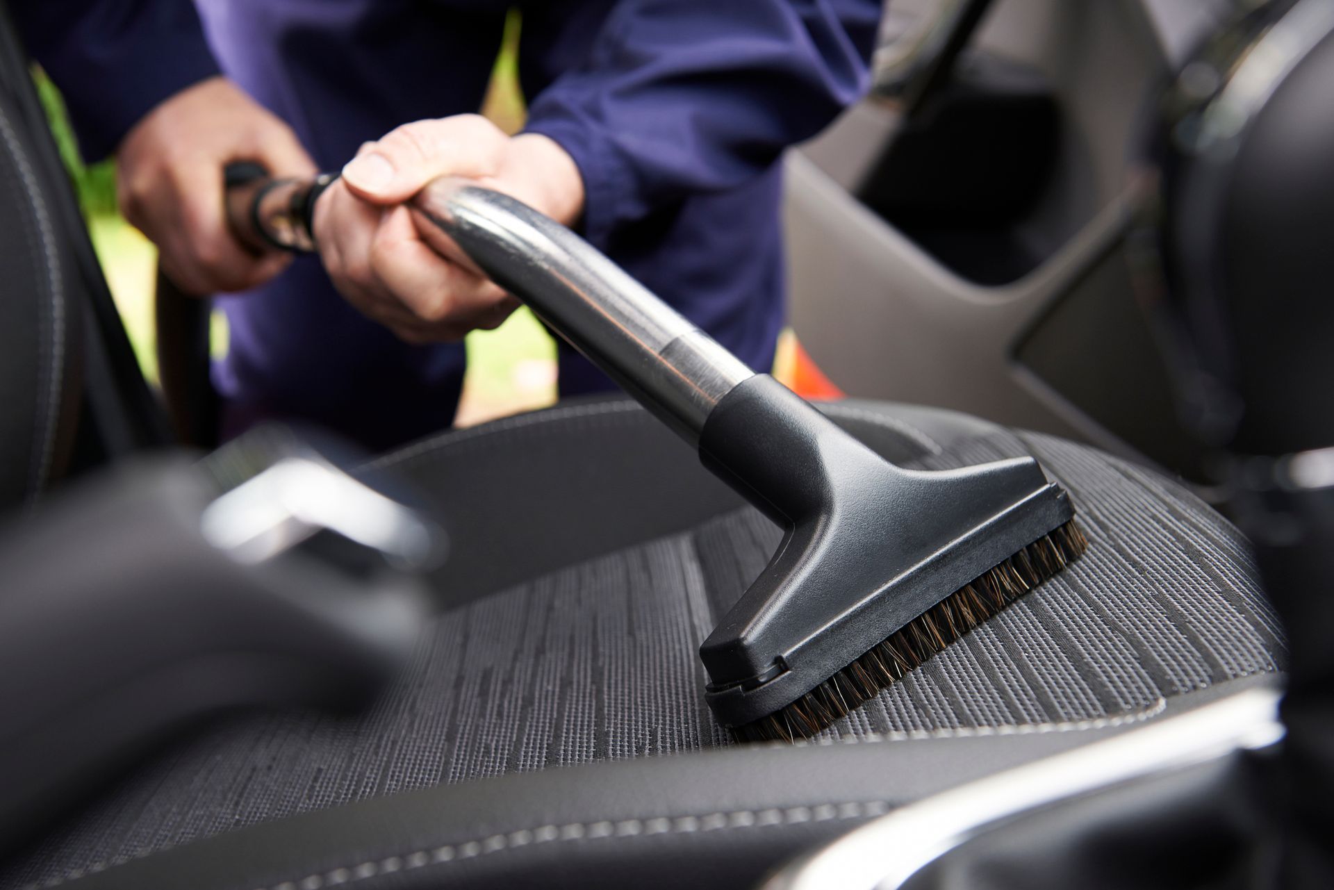 A person is cleaning the seats of a car with a vacuum cleaner.