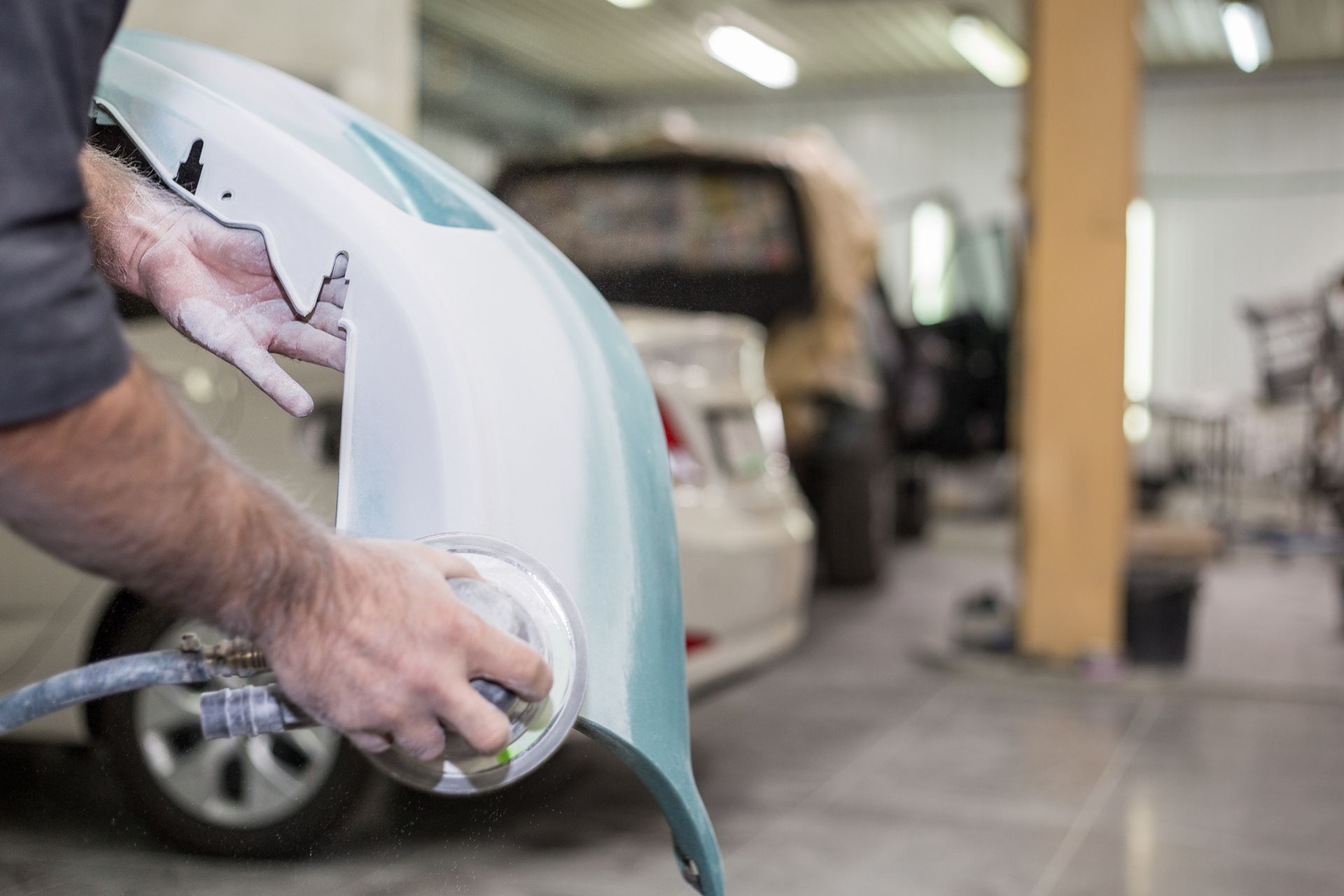 A man is painting a car bumper in a garage.