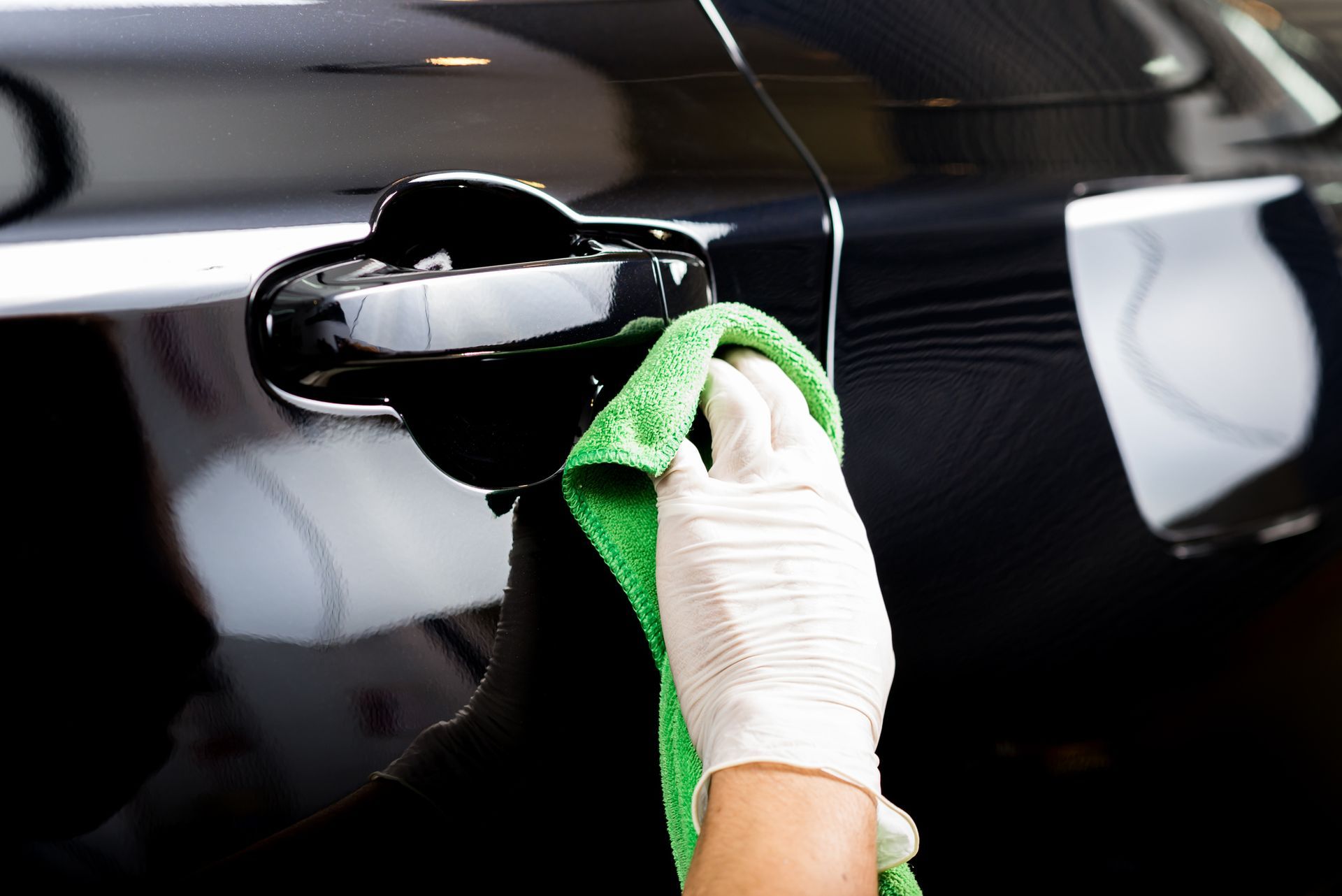 A person is cleaning the door handle of a car with a green towel.