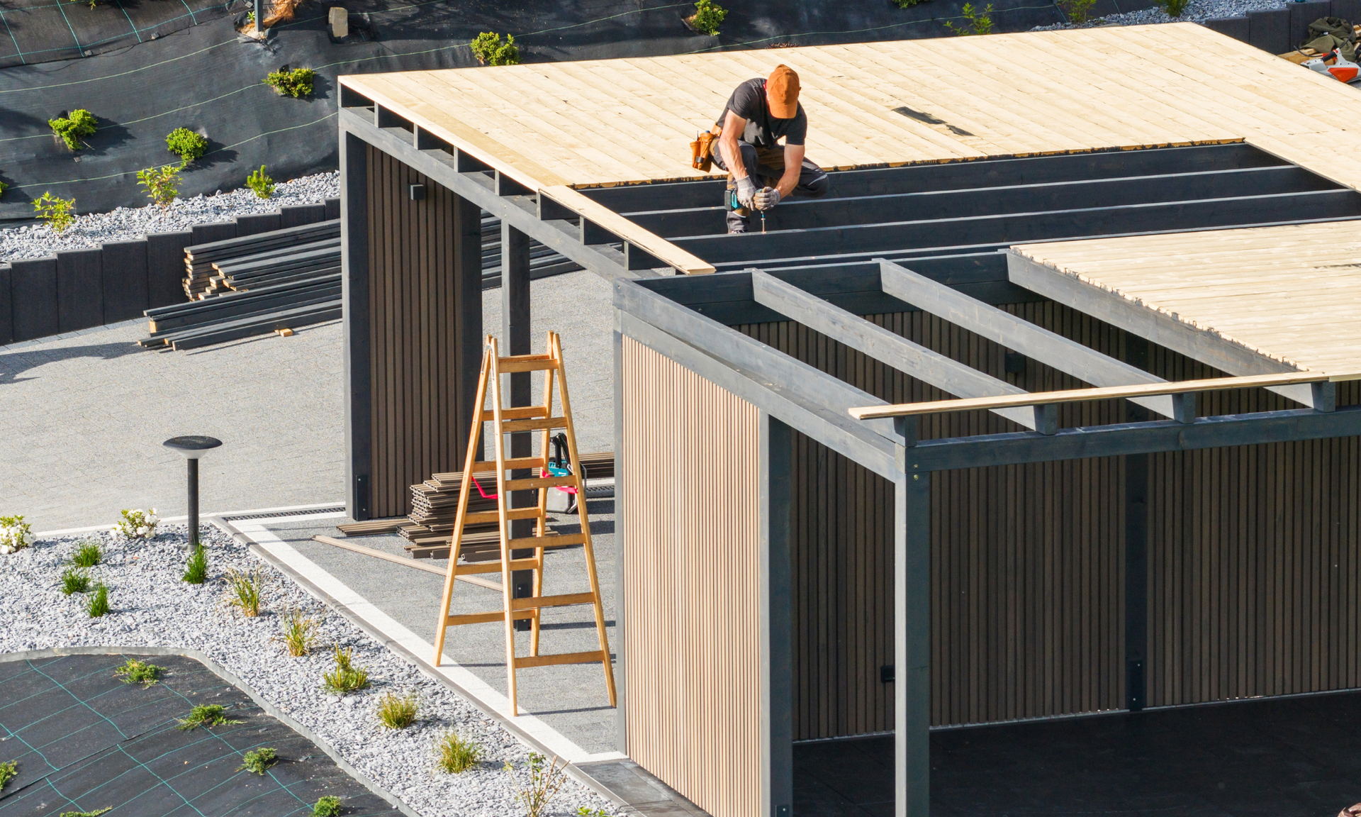 Een man is bezig met het bevestigen van houten planken op het dak van een moderne pergola. 