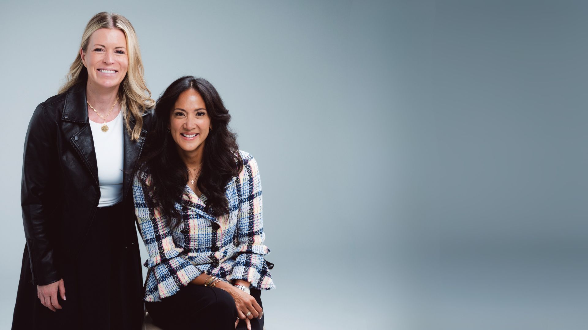 Dr. Woo and another smiling women, one standing, one seated, against a gray gradient background.