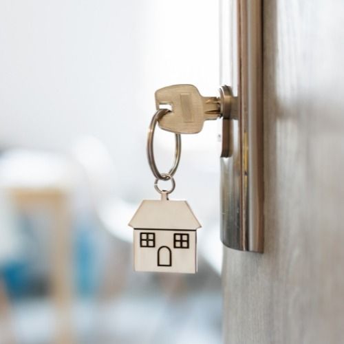 House-shaped keychain hanging from a door lock on a wooden door