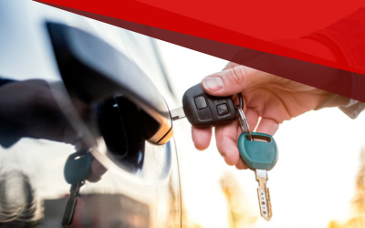 Hand holding car key fob near a car door handle, with a blurred vehicle in the background