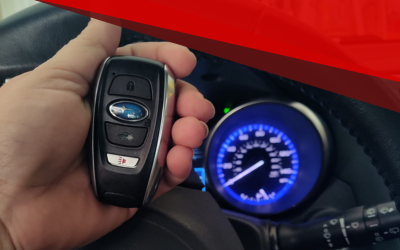 Hand holding a Subaru key fob beside a blue-lit car dashboard gauge