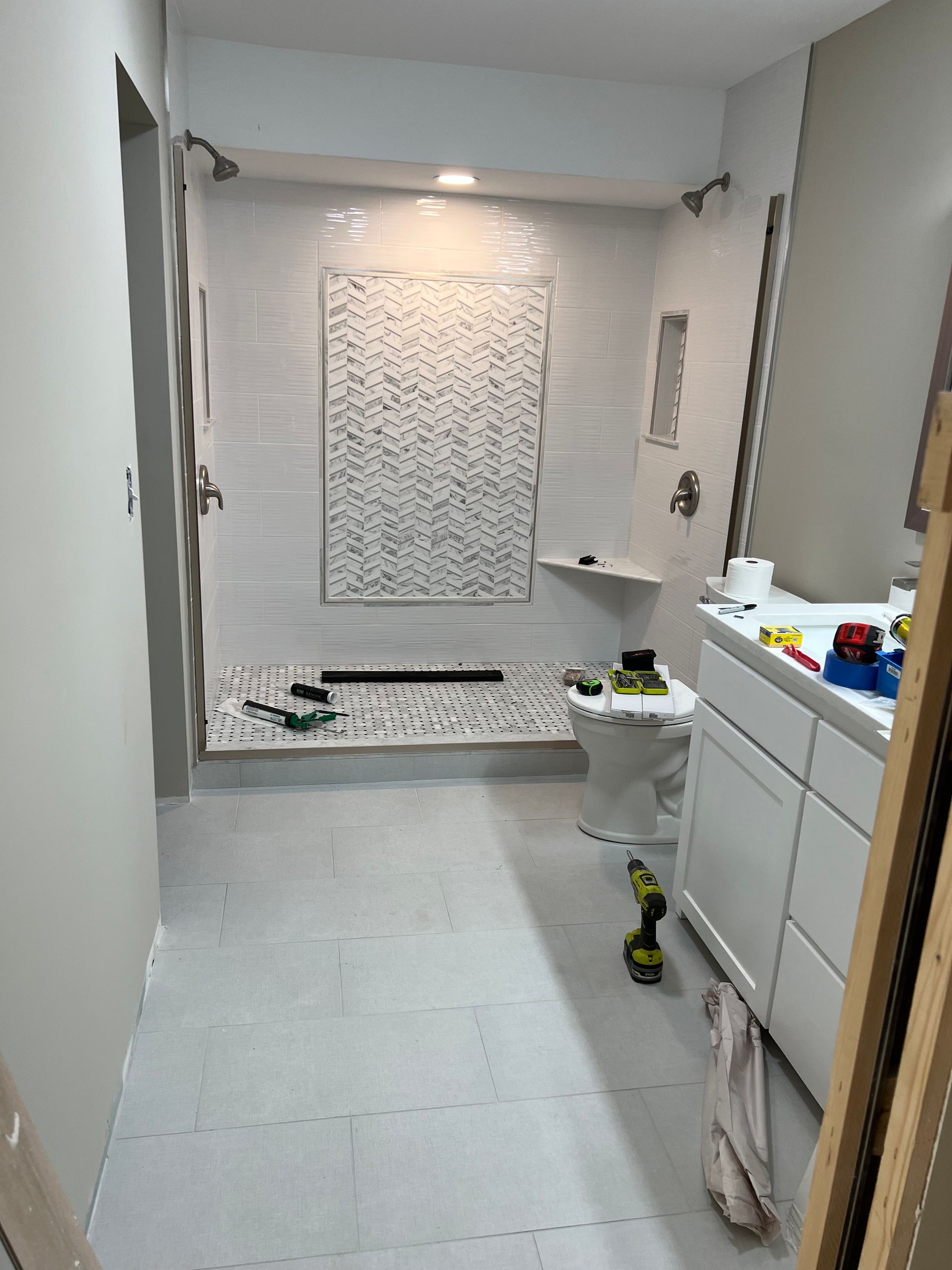 Bathroom with white tiles, shower with pebble floor, and white vanity.