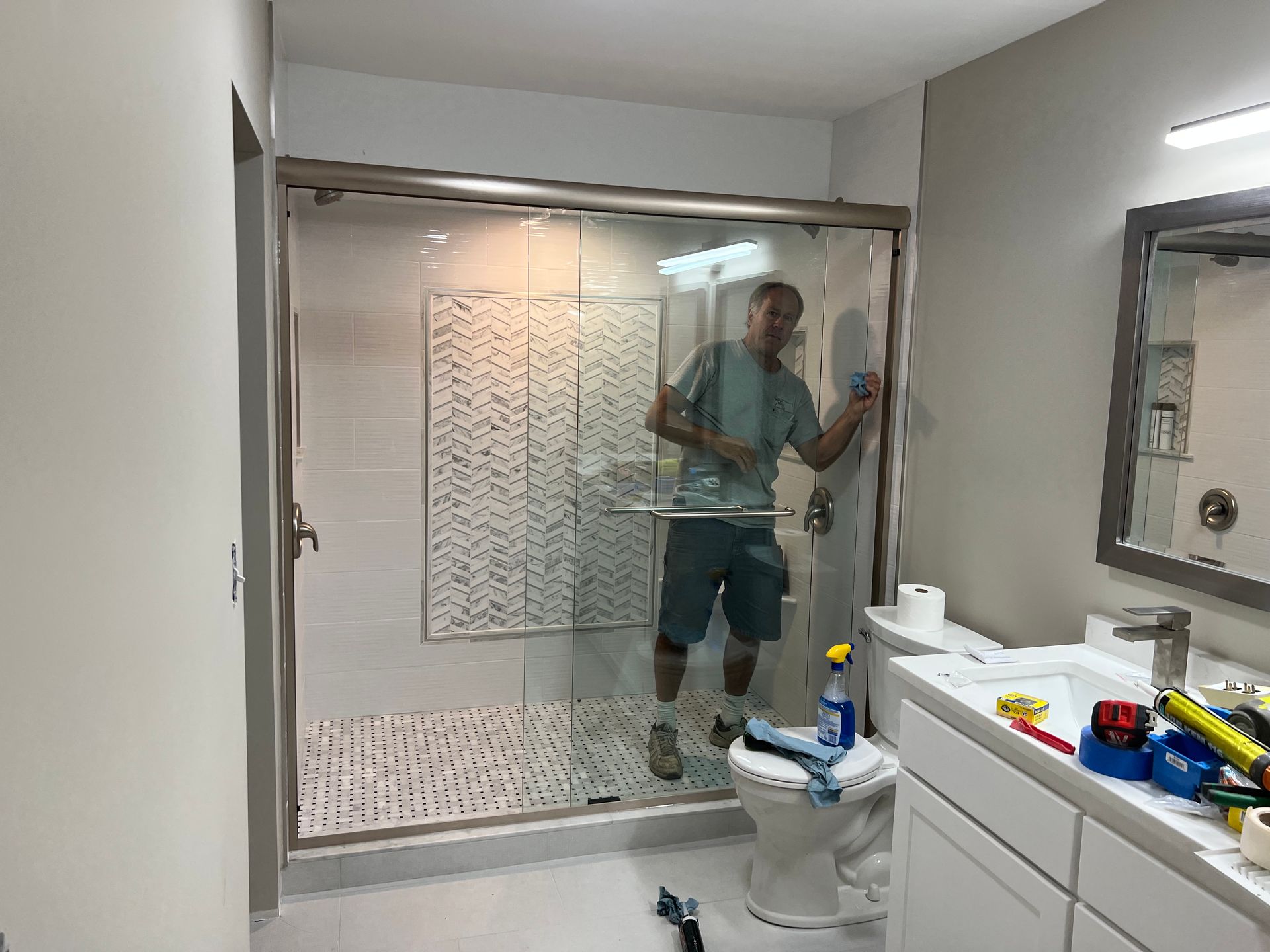 Person inside a newly renovated bathroom, working on the glass shower door.
