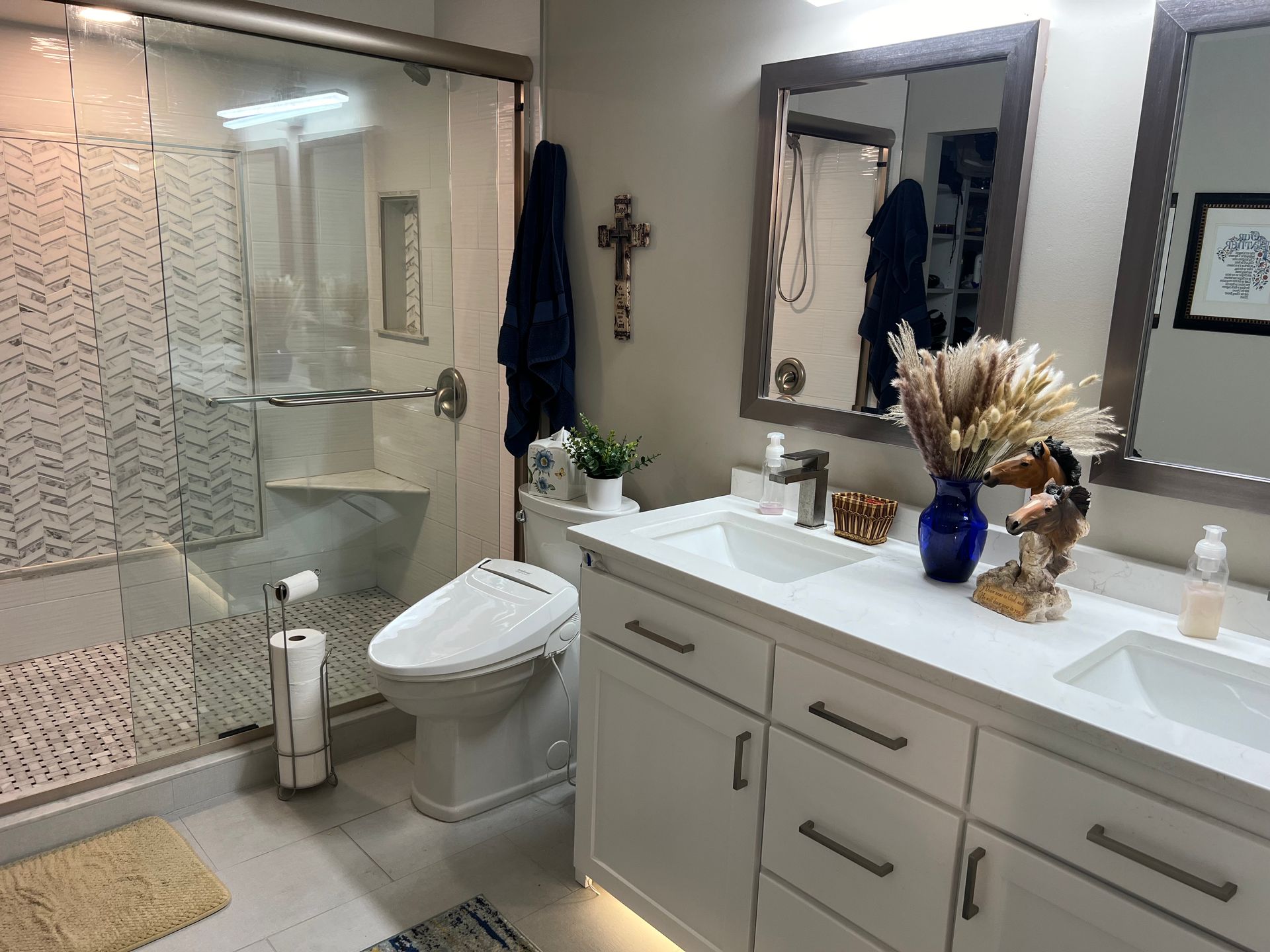 Modern bathroom with white cabinetry, double sinks, walk-in shower, toilet, and decorative elements.