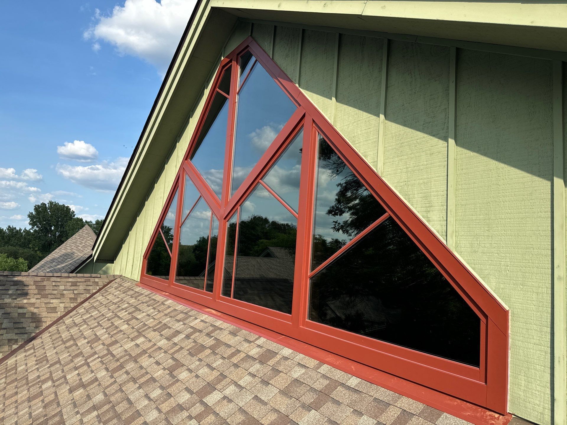 Triangular window with red trim on a green house, set against a blue sky.